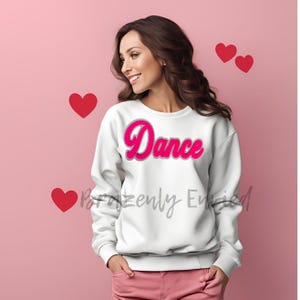 May include: White sweatshirt with a pink "Dance" graphic on the front. The sweatshirt is worn by a person with long brown hair. The background is pink.