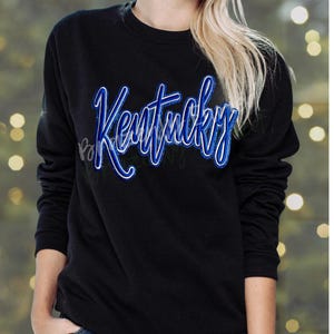 May include: Black crew neck sweatshirt with the word "Kentucky" in blue script lettering. The lettering has a white outline. The sweatshirt is a long-sleeved top.