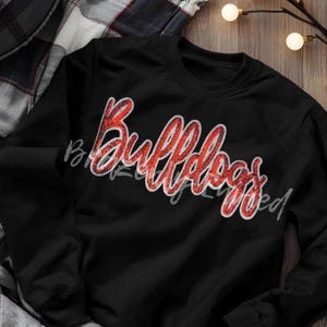 May include: Black sweatshirt with the word "Bulldogs" in red glitter script across the front. The sweatshirt has long sleeves and a crew neck. The word "Bulldogs" is outlined in white.