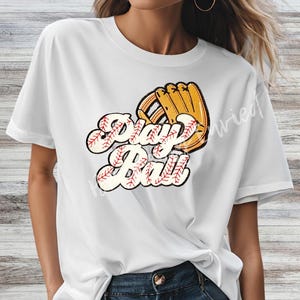 May include: White t-shirt featuring a baseball glove and the words "Play Ball" in a retro font. The text is designed to look like baseballs. The baseball glove is tan and brown. The shirt is a casual, everyday wear item.