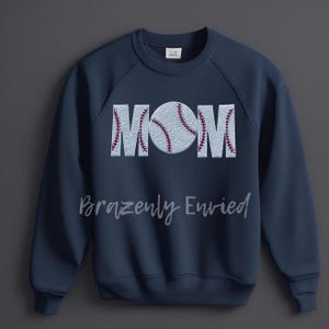 May include: Navy blue sweatshirt with the word "MOM" spelled out in white with a baseball graphic in the center. The baseball is white with red stitching.