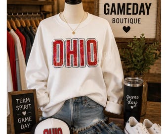 May include: A white long-sleeve sweatshirt featuring the word OHIO in red sequined block letters with silver outlines. The sweatshirt is paired with blue denim shorts, a white and black baseball cap with OHIO in red, and white sneakers.