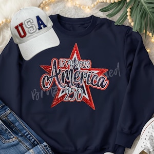 May include: A navy blue sweatshirt with a red and white star design that says "America 250" and a white baseball cap with "USA" in red and blue lettering. The sweatshirt and hat are patriotic themed.