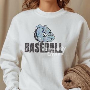 May include: White sweatshirt featuring a glittery blue bulldog graphic above the word "BASEBALL" in black block letters. The sweatshirt has long sleeves and a crew neck.