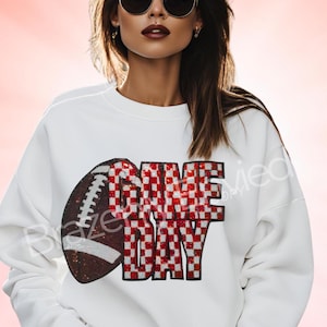 May include: White sweatshirt with a sequined football and the words "GAME DAY" in red and white checkered pattern. The football is brown and white. The sweatshirt is a casual, sporty style.