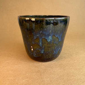 May include: A ceramic planter with a glossy finish. The dark green and blue glaze drips down the sides, creating a textured appearance. The vessel has a wide opening and a slightly tapered shape. The planter is suitable for indoor or outdoor use.