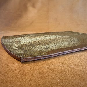 May include: A rectangular ceramic serving platter with a rounded edge. The platter has a mottled, textured surface with shades of brown and tan. The edges are a darker brown.