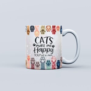 Pu&ograve; includere: Tazza in ceramica bianca con manico curvo. La tazza presenta un disegno di colorate zampe di gatto sul bordo e il testo "CATS make me Happy YOU? not so much" in nero. L'articolo &egrave; a tema gatto.