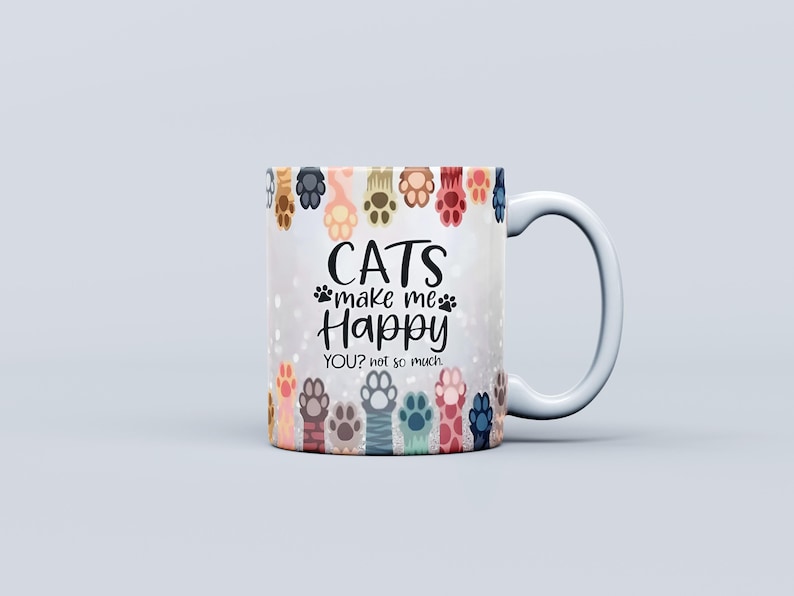 Pu&ograve; includere: Tazza in ceramica bianca con manico curvo. La tazza presenta un disegno di colorate zampe di gatto sul bordo e il testo "CATS make me Happy YOU? not so much" in nero. L'articolo &egrave; a tema gatto.