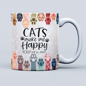 Pu&ograve; includere: Tazza in ceramica bianca con un design avvolgente con impronte di zampe di gatto colorate e la scritta "CATS make me Happy YOU? not so much." La tazza ha un manico bianco ed &egrave; adatta a bevande calde o fredde.