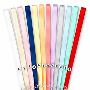 May include: A collection of colorful satin ribbons in various shades, including white, pink, blue, yellow, and red. Each ribbon has a small, decorative button with a black and white design. The ribbons are arranged in a fan shape.