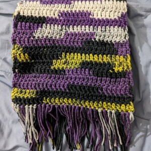 May include: A crocheted scarf with a fringe in shades of purple, black, white, and yellow.