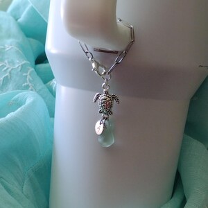 May include: A silver chain bracelet with a silver turtle charm and a light blue glass bead. The bracelet has a lobster clasp.