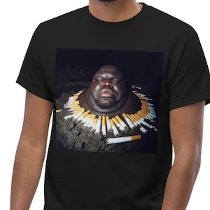 May include: A black t-shirt featuring a graphic print of a person's head surrounded by cigarettes.