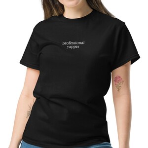 May include: Black t-shirt with the text "professional yapper" in white lettering.