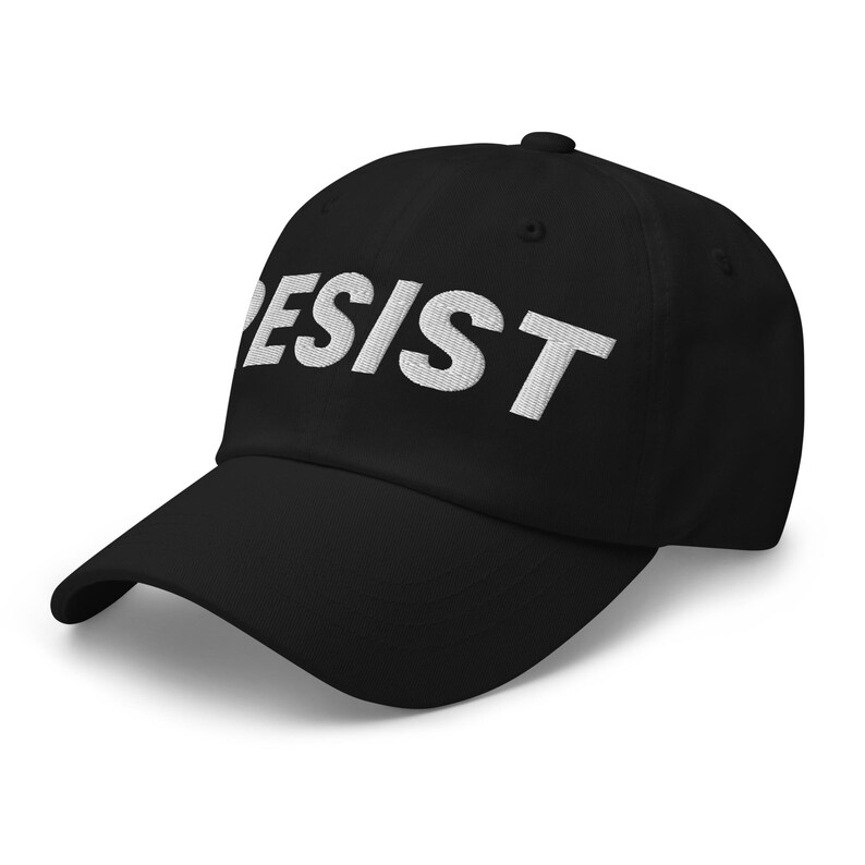 K&ouml;nnte beinhalten: Schwarze Baseballkappe mit dem Wort "RESIST" in Wei&szlig; auf der Vorderseite gestickt. Die Kappe hat einen gebogenen Schirm und ein klassisches sechsteiliges Design.