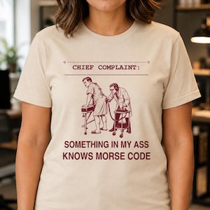 Puede incluir: Una camiseta beige de manga corta con una ilustración gráfica de color rojo oscuro de un médico examinando a un paciente. El texto dice CHIEF COMPLAINT: SOMETHING IN MY ASS KNOWS MORSE CODE. El diseño está centrado en la parte delantera.