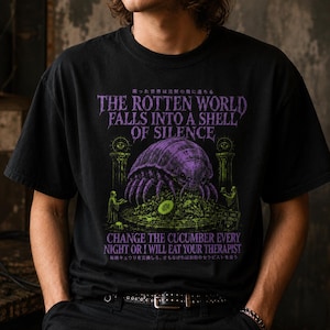 Könnte beinhalten: Ein schwarzes T-Shirt mit einer violetten und grünen Grafik eines großen Isopoden auf einem Podest. Der Text lautet: THE ROTTEN WORLD FALLS INTO A SHELL OF SILENCE, CHANGE THE CUCUMBER EVERY NIGHT OR I WILL EAT YOUR THERAPIST, sowie japanische Schriftzeichen.