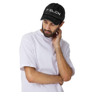 May include: A black distressed baseball cap with white embroidered text that reads "FELON".