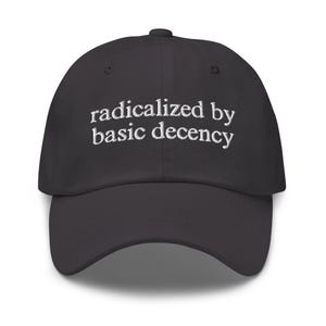 May include: A dark grey baseball cap featuring the embroidered phrase "radicalized by basic decency" in white. The cap has a curved peak and a button on top. A fashionable accessory for casual wear.