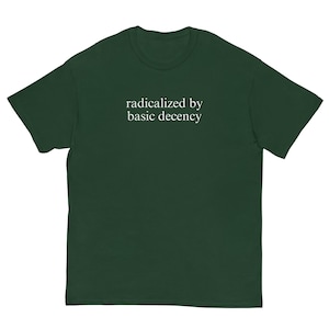 Puede incluir: Una camiseta verde oscuro con la frase blanca "radicalized by basic decency". La camiseta tiene cuello redondo y mangas cortas.