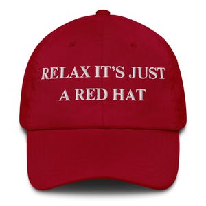 Puede incluir: Gorra de béisbol roja con la frase bordada en blanco "RELAX IT'S JUST A RED HAT". La gorra tiene una visera curva y una correa ajustable en la parte trasera.