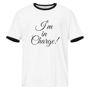 May include: White t-shirt with black trim on the collar and sleeves. The shirt displays the text "I'm in Charge!" in black, elegant script. The design is centered on the front of the shirt.