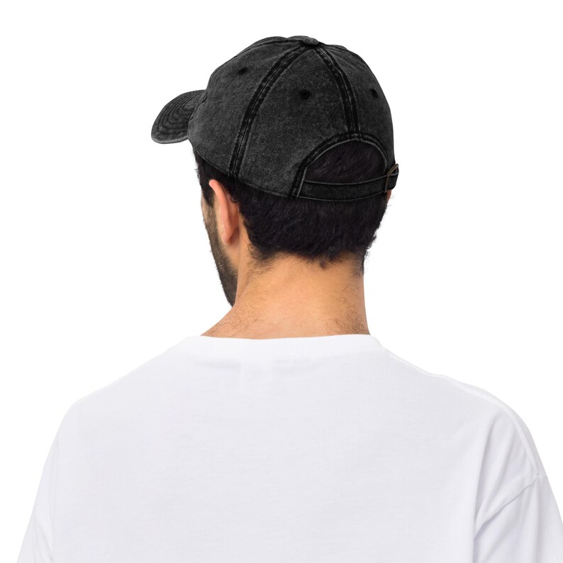 May include: A black denim baseball cap with a slightly distressed look. The cap has a curved brim and a back strap with a buckle.