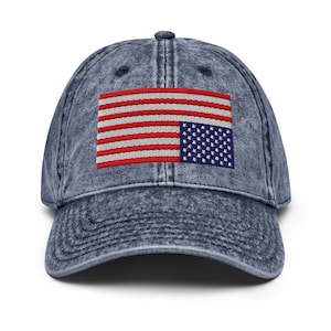 May include: A blue denim baseball cap with a distressed look. The cap features an embroidered American flag with the stars and stripes reversed.