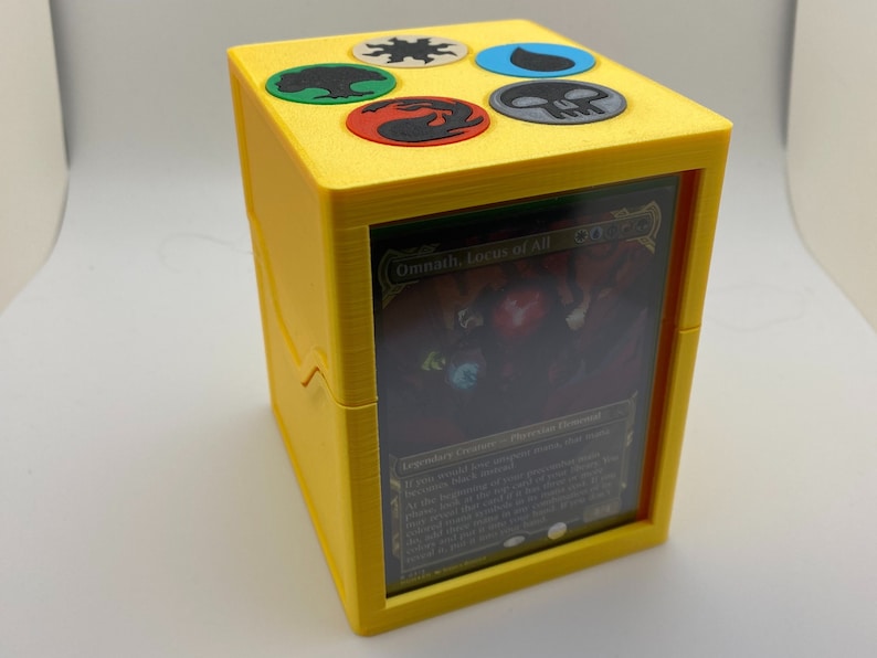 May include: Yellow card deck box with a clear window showing a Magic: The Gathering card with the text "Omnath, Locus of All". The top of the box has five colored symbols.