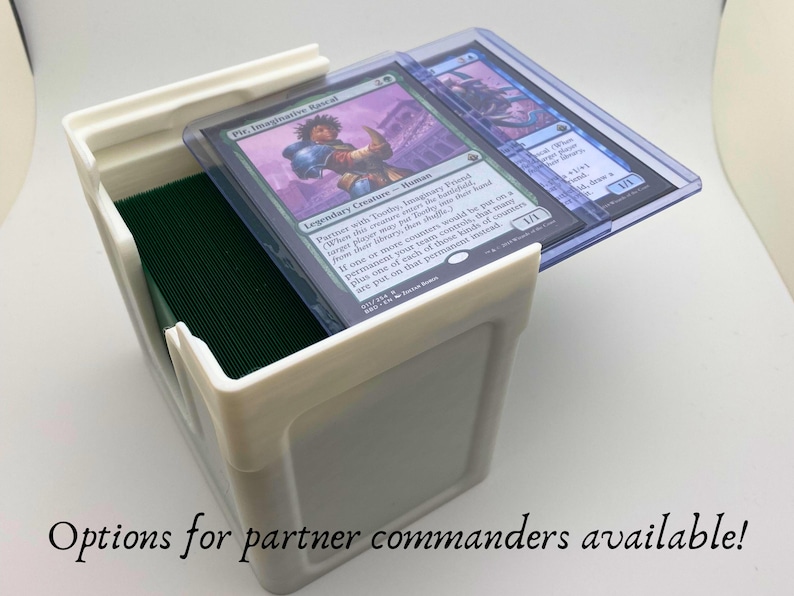 May include: White plastic card storage box with a green felt liner. Two Magic: The Gathering cards are visible, one with the text "Vie, Imaginative Rascal" and the other with the text "Legendary Creature - Human". The text "Options for partner commanders available!" is visible at the bottom of the image.