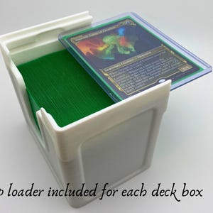 May include: White plastic deck box with a green deck of cards inside. A clear plastic top loader with a Magic: The Gathering card is on top of the box. The card is "Legendary Creature - Elemental".