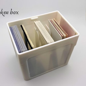 May include: White plastic box with the text "Token box" printed on the front. The box is filled with stacks of cards.