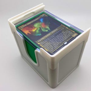 May include: White plastic card holder with a green insert. The top of the holder has a clear plastic cover and a Magic: The Gathering card is visible. The card is titled "Omnath, Locus of Creation" and is a Legendary Creature - Elemental.