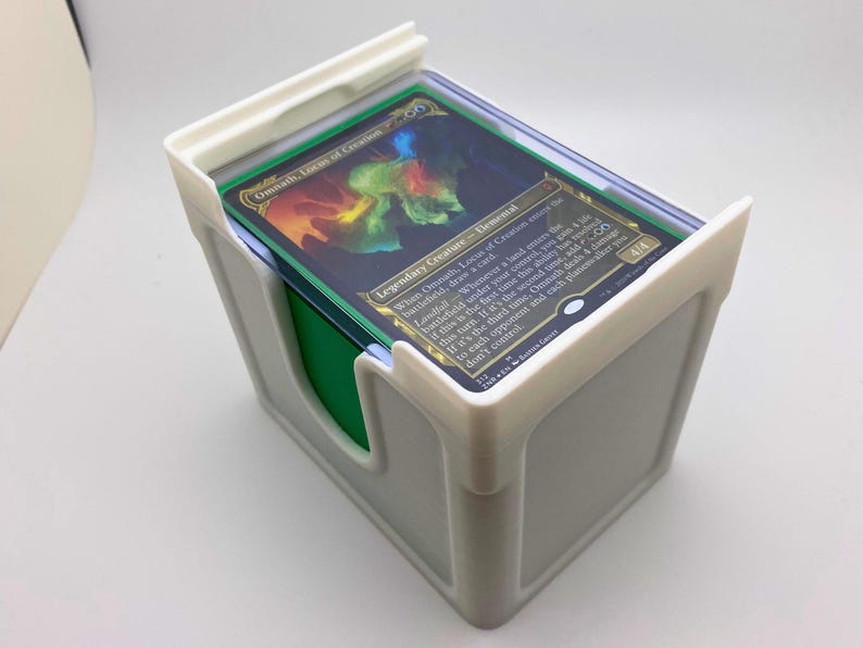 May include: White plastic card holder with a green insert. The top of the holder has a clear plastic cover and a Magic: The Gathering card is visible. The card is titled "Omnath, Locus of Creation" and is a Legendary Creature - Elemental.