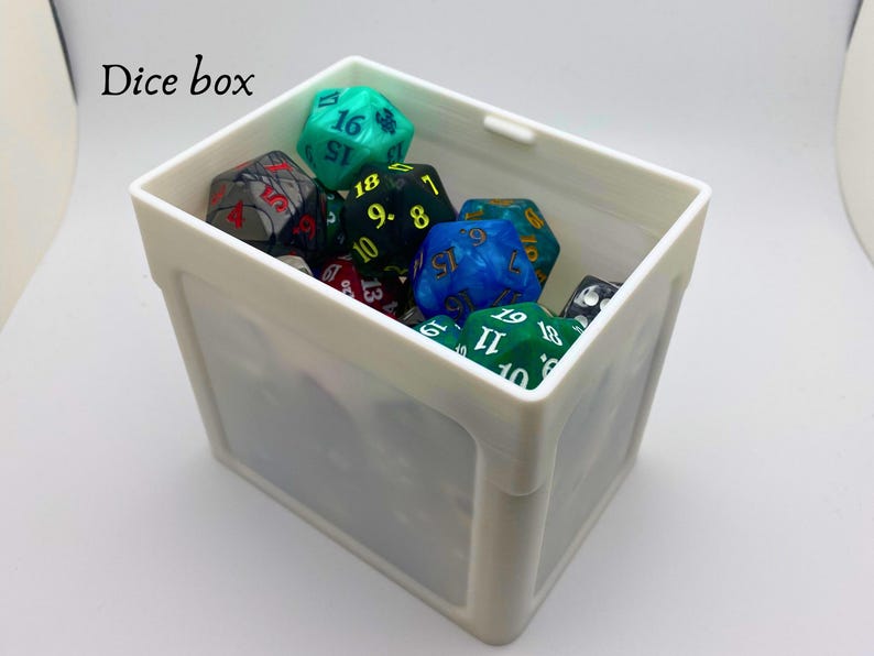 May include: A white plastic dice box filled with colorful dice. The dice have black and white numbers and some have green and blue swirls.