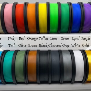 May include: A collection of 18 spools of filament for 3D printing in various colors, including beige, pink, red, orange, yellow, lime, green, royal blue, purple, sky blue, teal, olive, brown, black, charcoal gray, white, and gold.