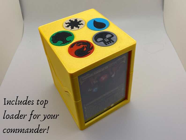 May include: Yellow cube-shaped card box with a clear window on one side. The top of the box has five colored circles with symbols representing the five elements of magic: fire, water, earth, air, and a skull. The text "Command Tower of All" is visible through the window.