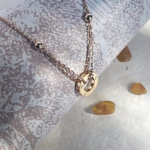 May include: A gold necklace with a circle pendant featuring small stones. The necklace has two chains and small round beads.
