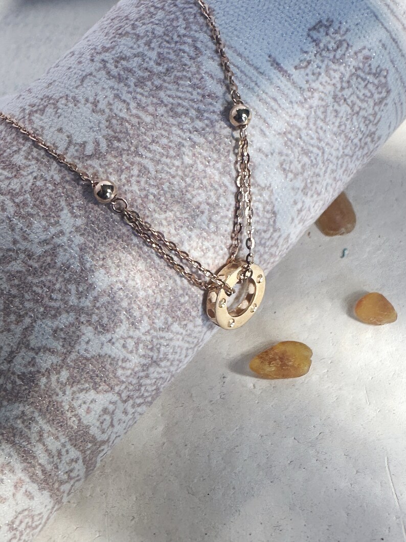 May include: A gold necklace with a circle pendant featuring small stones. The necklace has two chains and small round beads.
