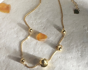 May include: A gold chain anklet with a heart charm and four round beads. The anklet has an adjustable length.