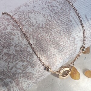May include: A gold chain necklace with a circular pendant featuring a circle of small diamonds. The necklace is on a white and brown textured surface.