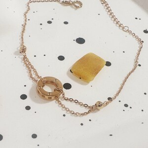 May include: A gold-toned chain bracelet with a circle pendant featuring a textured design. The bracelet has a lobster clasp closure.