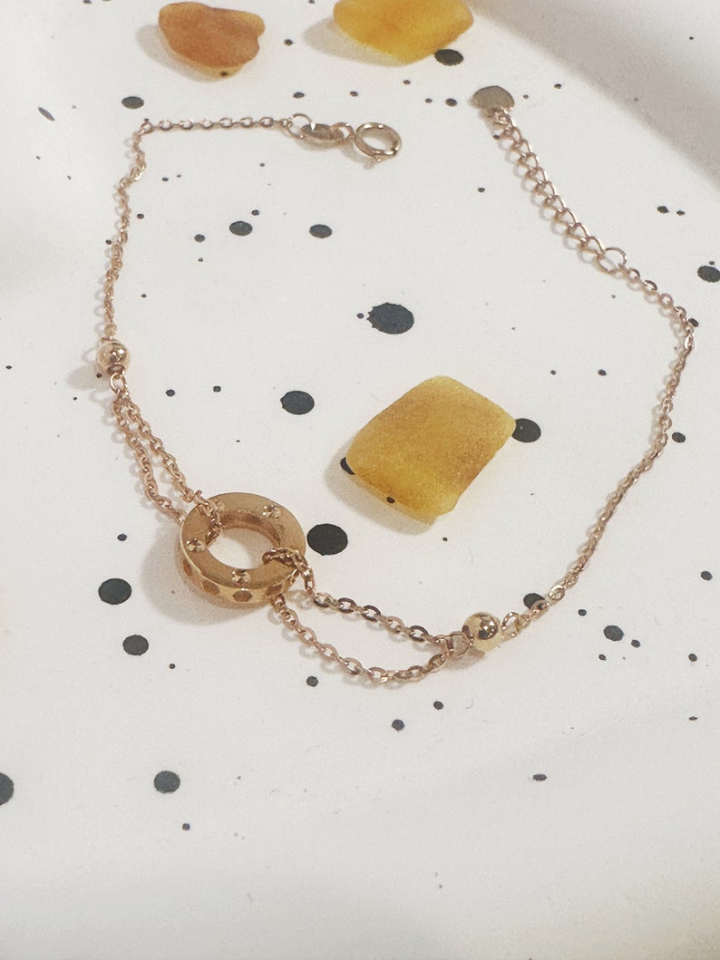 May include: A gold-toned chain bracelet with a circle pendant featuring a textured design. The bracelet has a lobster clasp closure.