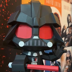May include: A black Darth Vader figure with red eyes and a red lightsaber. The figure has a geometric design and is holding the lightsaber in its right hand. The figure is a collectible item.