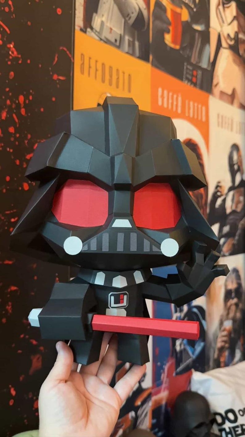May include: A black Darth Vader figure with red eyes and a red lightsaber. The figure has a geometric design and is holding the lightsaber in its right hand. The figure is a collectible item.