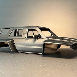 Könnte beinhalten: Eine matt dunkelgraue Modellauto-Karosserie mit kantiger SUV-Silhouette, breiten Kotflügelverbreiterungen, Frontgrill, Seitenspiegeln und offenen Fensterrahmen. Die Oberfläche weist eine für den 3D-Druck typische Textur auf.