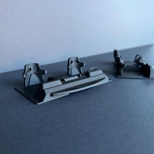 Könnte beinhalten: Schwarzes Miniatur-Rennwagen-Cockpit-Modell mit zwei Sitzen, einem Lenkrad und Armaturenbrettdetails. Das Modell besteht aus einem mattschwarzen Material und steht auf einer dunklen Oberfläche. Das Design ist detailliert und scheint 3D-gedruckt zu sein.