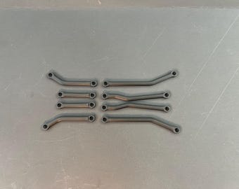 Puede incluir: Una colección de pequeñas varillas metálicas curvas y rectas con agujeros en cada extremo, dispuestas sobre una superficie gris. Las varillas son de color gris oscuro y parecen ser componentes de un objeto o máquina más grande.