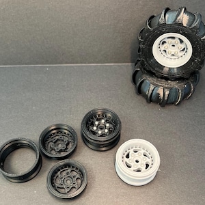 May include: An assortment of black and white model car wheels. Two assembled wheels with black tires and white centers are stacked. Several disassembled black wheels and a single white wheel are also present.